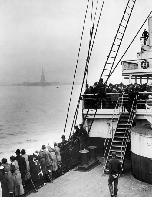 Immigrants on a ship approaching New York City, bound for Ellis Island, with the Statue of Liberty in the background.