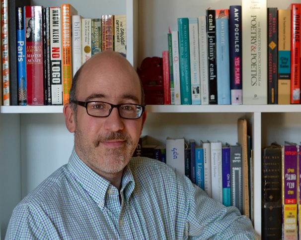 Man wearing glasses smiles in front of bookcase