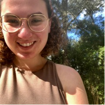 Girl in glasses smiles at camera in front of trees and blue sky