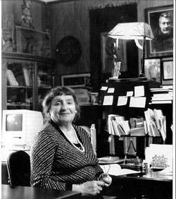 Photo of Chava Rosenfarb sitting at a desk holding glasses, in black and white
