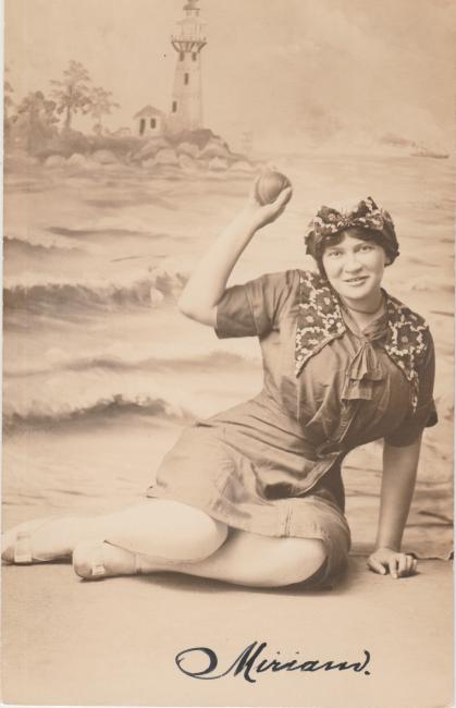 Studio portrait of Miriam Karpilove in a beach outfit holding a ball, sitting in front of a fake beach backdrop.