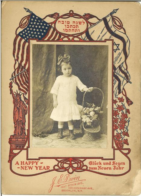 Rosh-Hashana greeting card with a photo of a young child and a basket of flowers bordered by American and Zionist flags and the Statue of Liberty. Text reads: leshana tova tikoseyvu vetakhateymu, a happy new year, Gluck un Segen zum neuen Jahr, J. E. Dwin, 1697 Pitkin Ave., cor. Rockaway Ave., Brooklyn, N.Y.