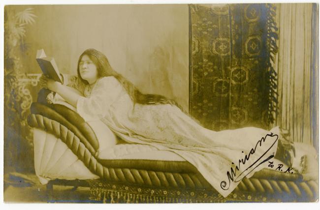 Sepia-toned photograph of Miriam Karpilove wearing a white flowing dress, with long brown hair reading a book while reclining on a chaise-lounge. Text reads: Miriam, to R. R.