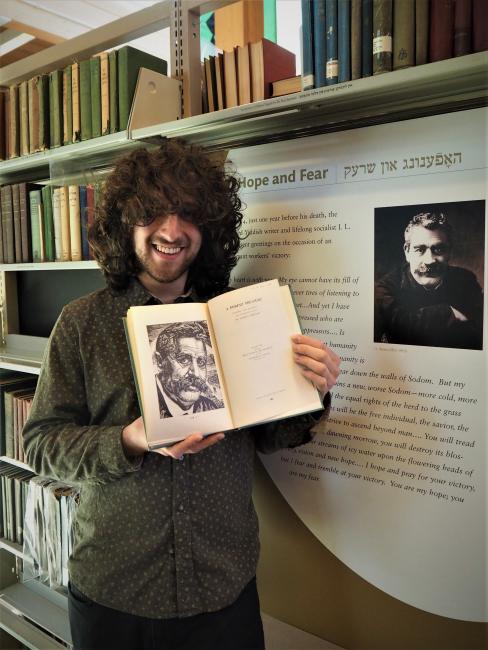 Joseph, white man with long curly dark brown hair, holds a book open to an illustration of I. L. Perets
