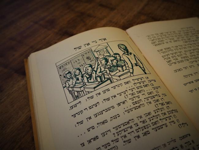 Page in a Yiddish learning book with an illustration depicting students in a classroom.