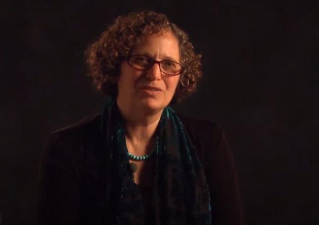 Woman with short curly hair and glasses against dark background