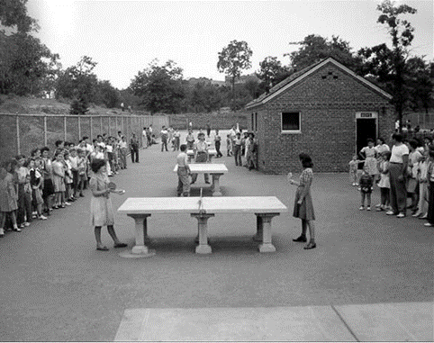 Two players challenge each other to ping-pong, with onlookers behind