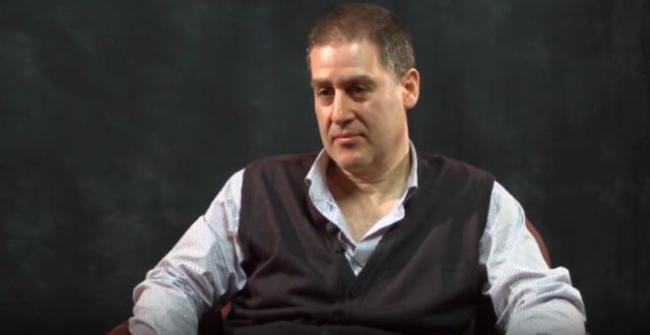David Mazower sits wearing a grey vest and blue striped button-down shirt.