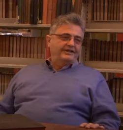 Samuel Kassow wears purple sweater and glasses, and sits in front of book shelves