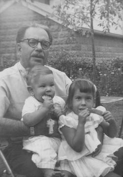 A man with glasses sits outside with a young boy and girl on his lap