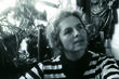 Grace Paley gazes into the distance in front of some plants. Black and white image.