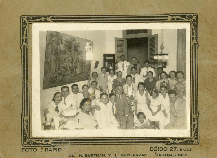 A group of adults and children pose in a living room, with a boy in the center wearing a prayer shawl