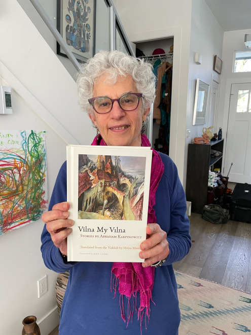 Woman wearing glasses and pink scarf holds up book, "Vilna My Vilna"