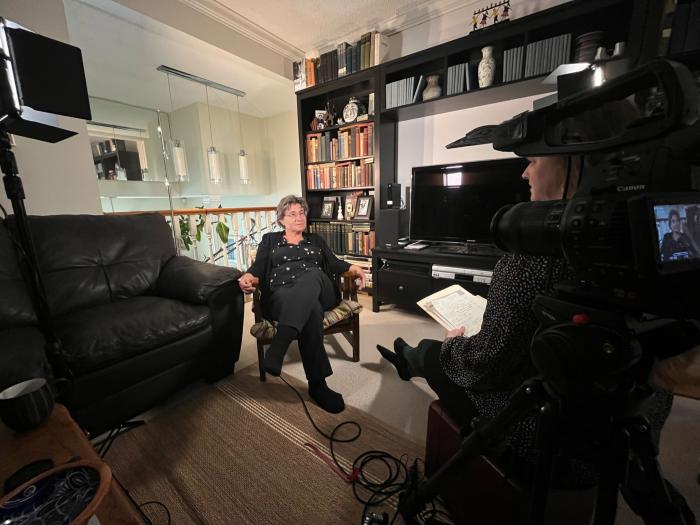 Christa Whitney interviews a woman wearing black and sitting in front of a leather sofa