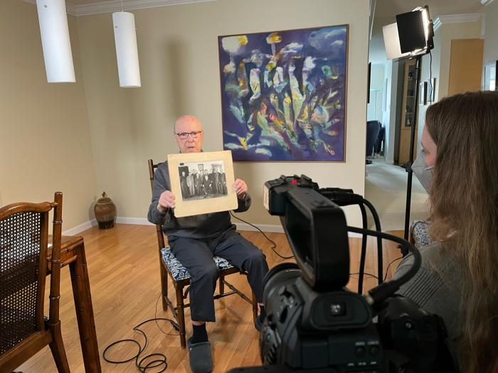 Man holds up an old photograph while being interviewed