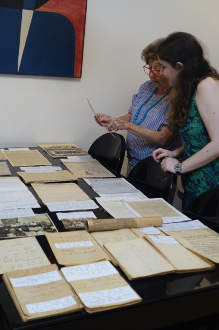 Two women stand next to a table filled with old documents.