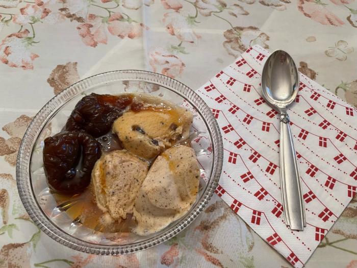 Rum raisin ice cream and baked figs in a bowl on a table-cloth covered table. Silver spoon rests next to it.