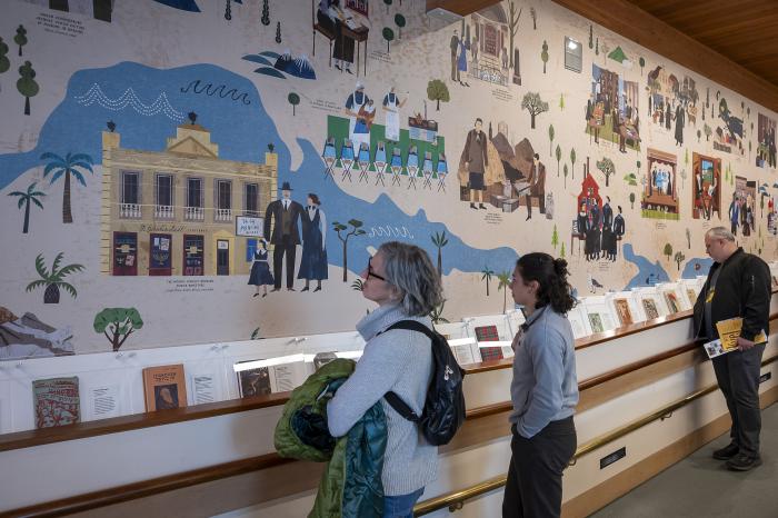 Three museum visitors observe a large mural titled "Yiddishland"