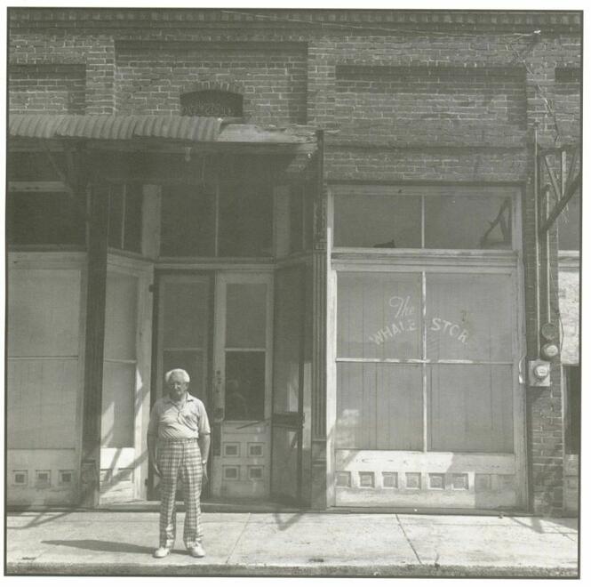 Aaron Kline in front of The Whale Store, Alligator. High-waisted pants-wearing elderly gent in front of a brick-facade store
