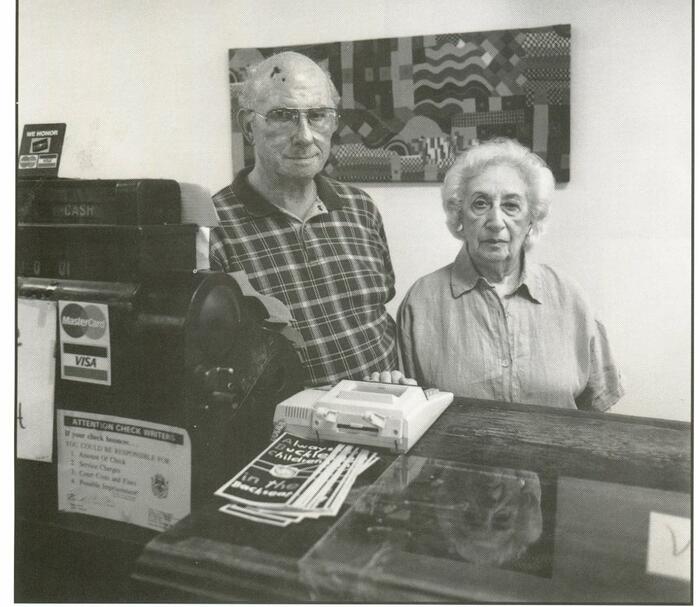 Melvin and Maureen Lipnick in Weinberg's, a children's store, Indianola. Elderly couple in front of a counter.