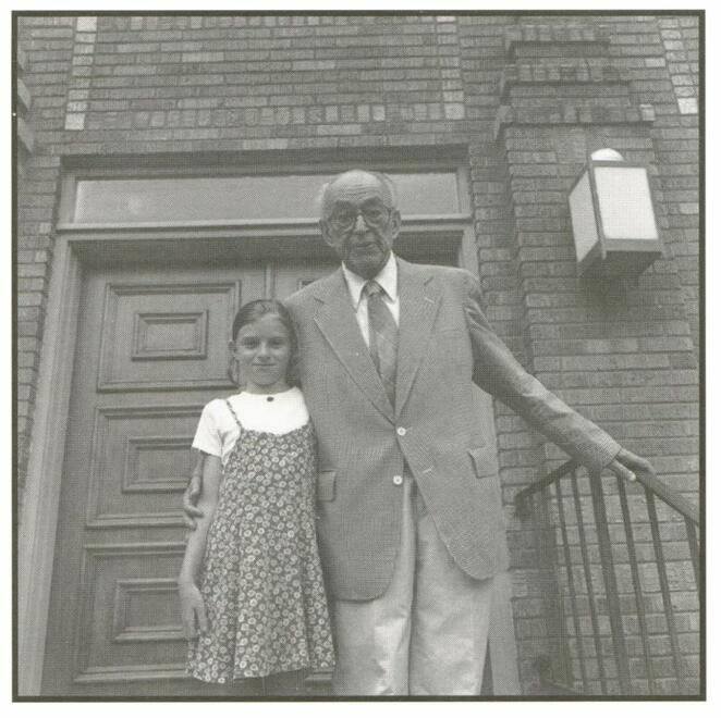 Rabbi Moses Landau and Melissa Chiz in front of the Adath Israel Temple, Cleveland, Mississippi. Elderly gentleman in suit, girl in dress, brick-facade synagogue.