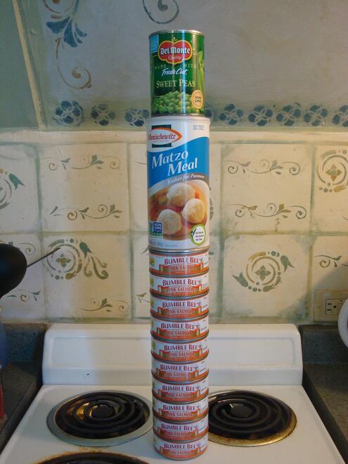 Cans of salmon and peas and a container of matzoh meal stacked up