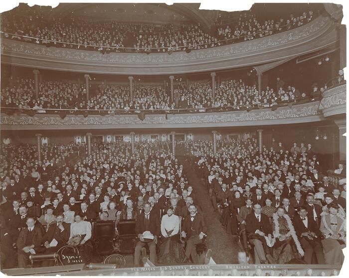 Sepia image of a large audience in the American Theatre, ca. 1902, all facing the camera.