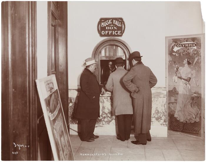 Three men standing at the box office of the Olympia Theatre, 1895, with a billboard featuring Yvette Luilbers visible.