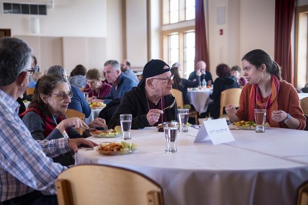 four people eating at round table, man with cap talks to woman in orange, smiling