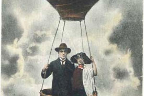 A man and woman stand in a hot air balloon basket against a cloudy backdrop, drawing