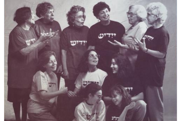 Group of women of all ages talk, wearing shirts that say "Yiddish," in Yiddish