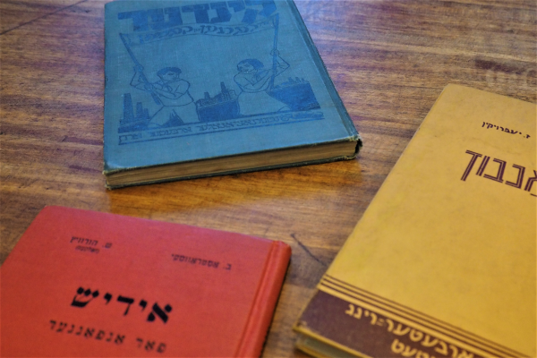 Three bright primary colored Yiddish books on a wooden table.